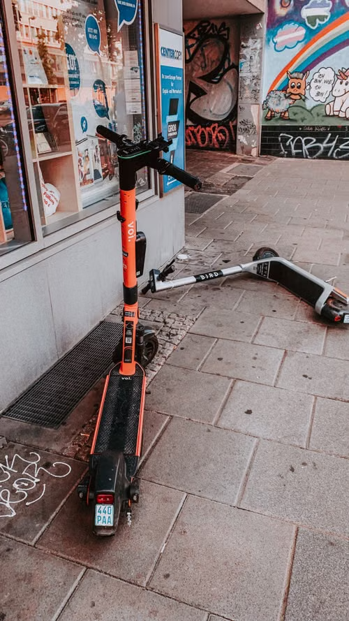Patinete elétrico caído na calçada ao lado de outro patinete elétrico em pé